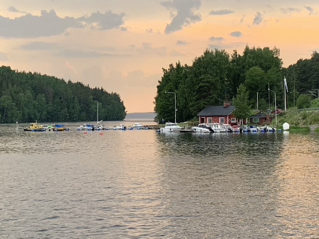 Yleiskuva Siuron satamasta: laiturit veneineen, punainen maja, vähän satamaan johtavaa tietä ja taustalla järveä saarineen.